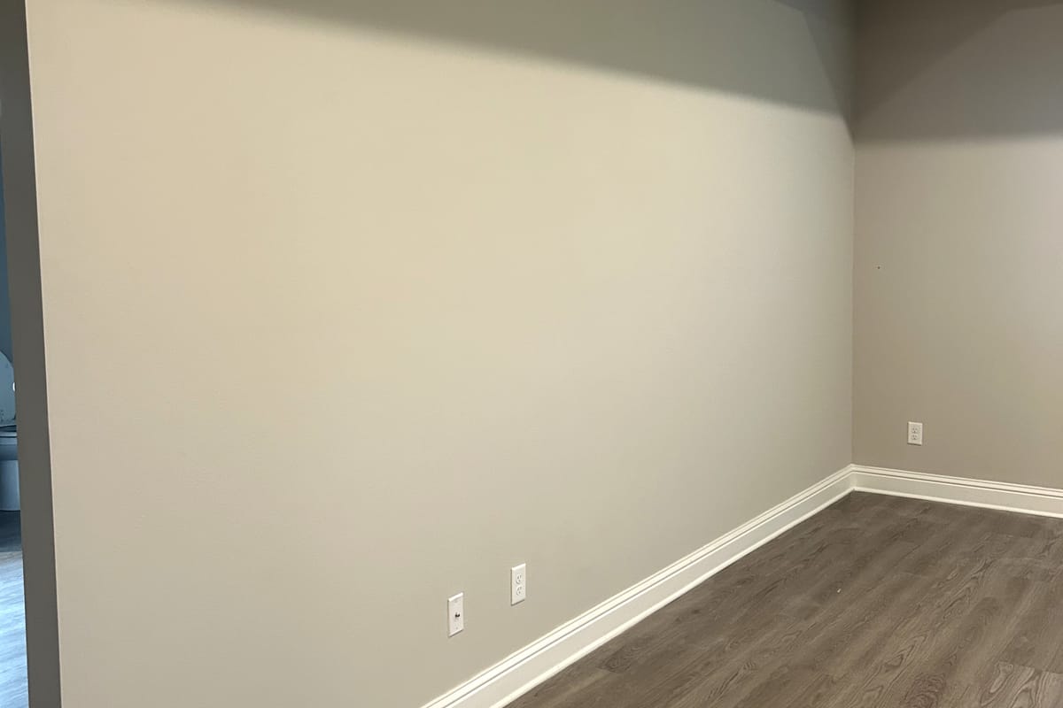 Empty room with a wall finished flat and smooth, white baseboard and a wood-look floor