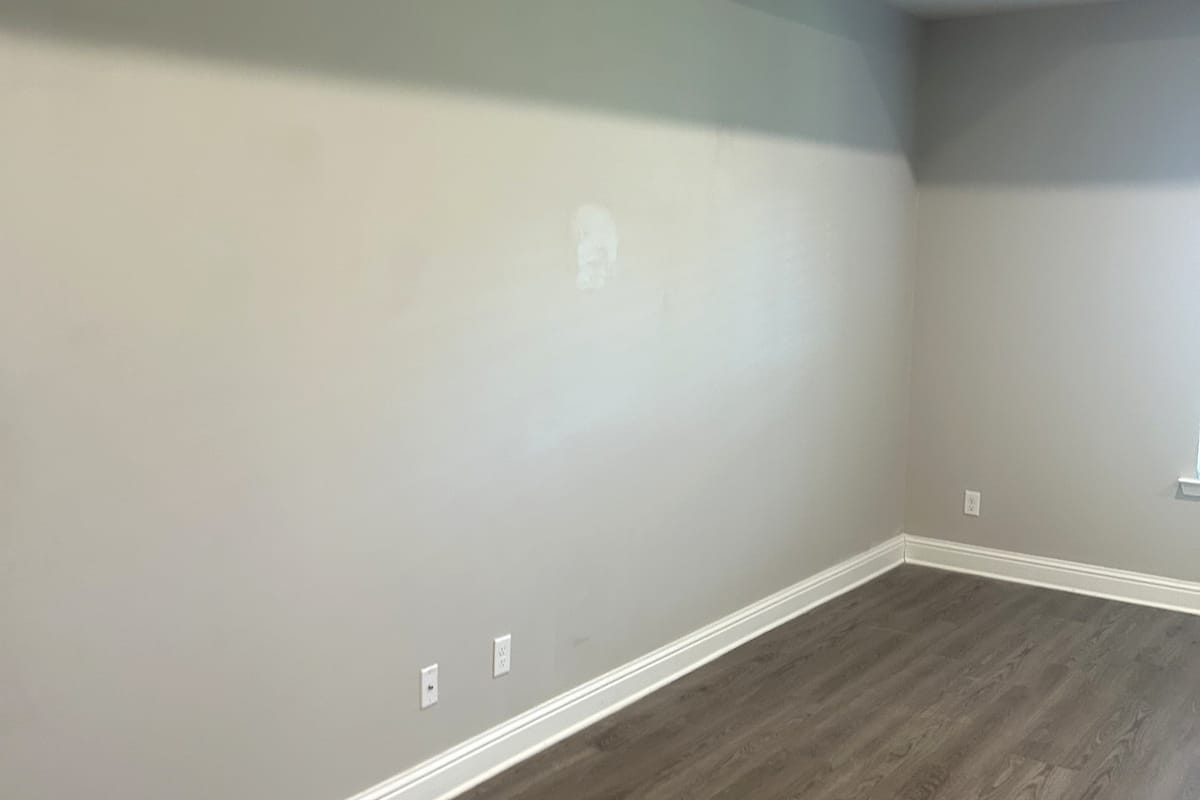 Interior wall with a drywall patch filled and sanded flush, ready for primer above a white baseboard