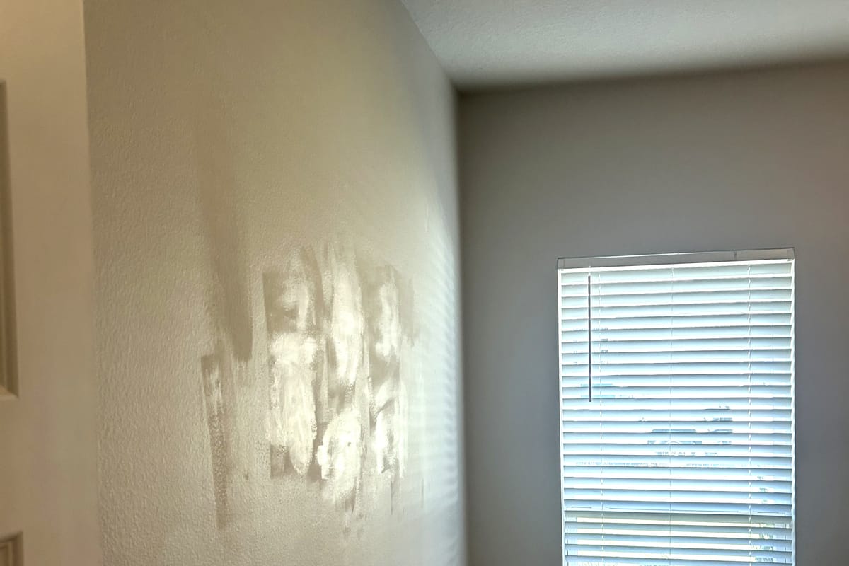 Drywall patches filled and sanded flat across an interior wall beside a blinded window